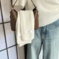 Detailansicht eines luxuriösen 100% Woll-Strickschals, elegant über einer braunen Handtasche. - Gebrochenes Weiß
