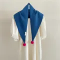 Nahaufnahme des blauen Strick-Dreieckschals aus Wolle mit verspielten rosa Bommel-Details. - Blau