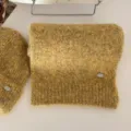 Vista detallada del conjunto de bufanda y gorro de punto amarillo suave con logo metálico. - Amarillo mostaza (bufanda)