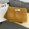 Gelber Strickwollschal Detail mit Markenetikett, gemütliches Wintermodeaccessoire. - Kurkuma
