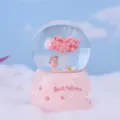 Close-up detail view of the pink crystal snow globe featuring an angel and cherry tree. - 5H133 Large Snowing with Lights & Music / Sitting Angel Girl