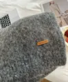 Gemütliches graues Strickschal-Detail mit weicher Alpakawolle und gebrandetem Lederetikett. - Meliertes Grau