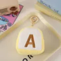 Close-up detail of cute plush letter coin purse with gold keychain and soft toast shape design. - Yellow