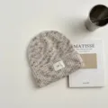 Vista detallada de un cómodo gorro de punto con textura de lana jaspeada y pequeña etiqueta. - Gorro Blanco Roto