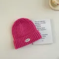 Gros plan détail d'un bonnet en tricot rose vif pour enfants avec un petit patch blanc de marque. - S / Rose rouge