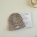Gros plan d'un bonnet en tricot douillet pour enfants en couleur kaki avec écusson. - S / Kaki