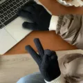 Close-up of black knitted touchscreen gloves with white ribbed cuffs on wooden desk detail. - One Size / Black