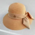 Gros plan d'un élégant chapeau de soleil en paille kaki avec nœud et logo métallique. - M (56-58cm) / Nœud Rose Clair