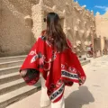 Detailed outdoor view of the red ethnic style winter shawl cloak, showing back pattern. - Tulip Red