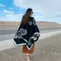 Detailed outdoor view of black knitted poncho with floral pattern, perfect travel style. - Large Flower Black