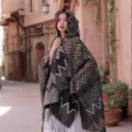 Detailed view of the ethnic style knitted hooded cape with zigzag pattern and fringe details. - Large Wave Hooded Poncho, Camel