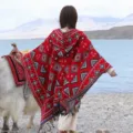 Detail view of women's ethnic style knitted hooded poncho cape with fringe and geometric patterns. - Triangle Pattern Hooded Poncho, Red