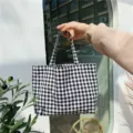 Close-up of a stylish black and white checkered canvas tote bag held by hand. - Black