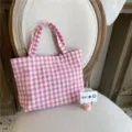 Vista detallada de un bolso de tela de cuadros vichy rosa y blanco sobre una silla de madera. - Rosa