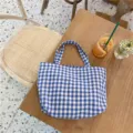 Close-up detail of a blue and white checkered canvas tote bag on a wooden cafe table. - Blue