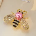 Détail exquis de broche abeille dorée, perle rose élégante et strass étincelants pour costume. - Base Bronze Violet