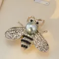 Detailed close-up of a charming crystal bee brooch with faux pearl head and rhinestones. - Silver Base Grey