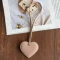 Detailed shot of pink PU leather heart bag charm and luggage tag on styled wooden surface background. - Pink