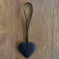 Vista detallada del dije de bolso en forma de corazón de cuero PU negro con textura y tira. - Negro
