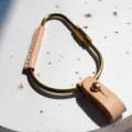 Close-up detail of brass carabiner keychain with PU leather wrap and metal rivet fastening. - Apricot