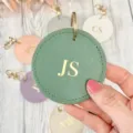 Closeup of round PU leather keychain with gold foil custom monogram letters detail. - Green