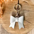 White PU leather bow keychain detail view, elegant gold hardware bag charm accessory key ring close up. - White