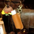 Detailed shot of vintage leather lip balm holder case with keychain, portable lipstick cover. - Tan
