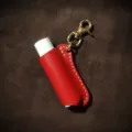 Detailed view of a red leather lipstick holder featuring a brass keychain and clasp for portable use. - Red