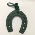 Detailed view of the green leather horseshoe bag charm with contrast white stitching and strap. - Green