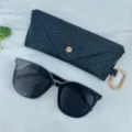 Close-up detail of black woven glasses case and stylish sunglasses with gold hardware. - Black