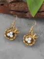 Close-up detail of vintage gold swallow bird nest pearl earrings, artistic nature design. - Antique Gold
