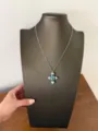 Detailansicht einer silbernen verzierten Kreuz-Halskette mit blau-grünem Kristallstein. - Kreuz Halskette (XL4761)