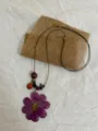 Detail shot of a long bohemian necklace featuring a purple pressed flower pendant and wooden beads. - Deep Purple Galsang Flower Style
