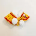 Close-up detail shot of cute handmade pet cape shawl featuring red trim and fluffy white pom-poms. - Yellow Lion Dance Shawl