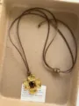 Closeup of vintage gold cross pendant necklace with heart gemstone and brown cord detail. - Gold Cross Pendant Style (XL1011A)