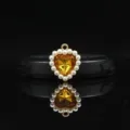 Detail view of the 18mm golden alloy heart pendant with sparkling yellow crystal and pearls. - Yellow