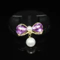 Primo piano dettagliato di un fiocco dorato con cristalli a cuore viola e perle pendenti. - Viola chiaro