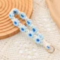 Llavero de pulsera con margaritas tejidas a mano en azul y blanco con aro dorado - Azul claro