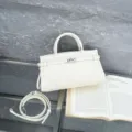 Detailed close-up of white leather Kelly handbag showcasing exquisite texture and strap. - Ivory