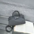 Dark grey leather handbag detail showcasing classic top handle and metal lock design. - Iron Grey