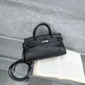 Black leather handbag detail view, retro top handle bag with metal lock and shoulder strap. - Black