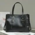 Detailed view of a black leather tote bag with metal buckle and shoulder strap. - Black