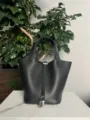 Vue détaillée du sac seau en cuir noir avec serrure argentée sur fond de marbre blanc. - Boucle Argentée / Noir