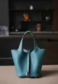 Detail van de blauwe lederen emmertas met premium textuur en een metalen hangslotje. - L18 B13 H18 cm / Denim blauw met zilveren gesp