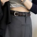 Détail en gros plan d'une ceinture en cuir marron pour femme avec boucle argentée sur pantalon. - Café