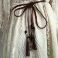 Détail de ceinture en corde tressée marron style bohème, avec glands et perles de bois. - Café