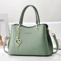 Détail de sac à bandoulière en cuir vert, cabas élégant avec charm cœur et pièces métal. - Vert