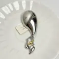 Detail view of silver metallic pepper tassel brooch with hanging charms on white plate. - Silver