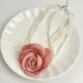 Detailopname van de meerlaagse parelketting met roze stoffen rozenbloemhanger voor dames. - Roze