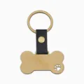 Detail en gros plan du porte-cles pendentif pour animal en forme d'os dore et cuir noir. - Patte Chien Ajourée Cuir Os Or